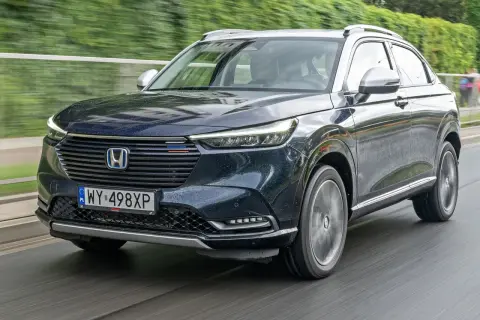 Ciemnogranatowy Honda HR-V na mokrej drodze. Nowoczesne reflektory i grill podkreślają jego dynamiczny charakter. Silniki tej generacji zapewniają oszczędność i płynność jazdy.