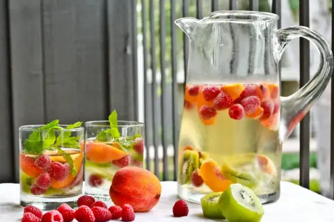 Orzeźwiająca sangria drink z malinami, brzoskwiniami i kiwi w dzbanku i szklankach, ozdobiona miętą.