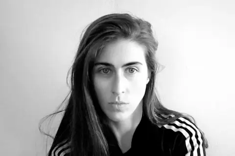 Ritratto in bianco e nero di Mara Oscar Cassiani, con lunghi capelli castani e indosso una felpa con le iconiche tre strisce.