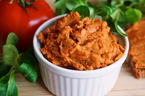 Pyszna, domowa pasta z soczewicy w białej miseczce, obok pomidora i świeżej zieleniny. Idealna na kanapki.