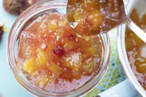 Ein Löffel voller glänzender Nektarinen Marmelade wird über ein Glas voller Fruchtstücke geschöpft.