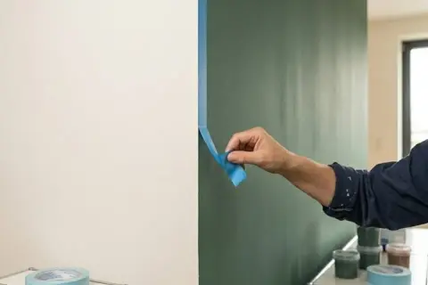Frau klebt mit blauer Klebefolie einen sauberen Rand, um die Wand streichen zu können.