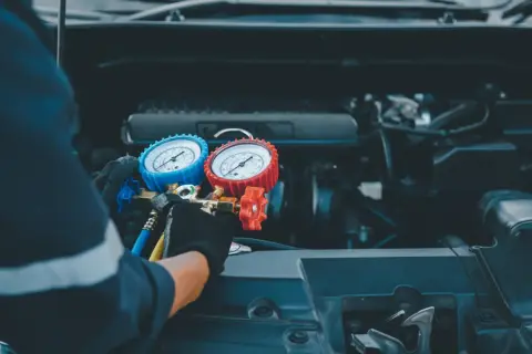 Tecnico con guanti controlla i manometri per ricaricare aria condizionata auto.