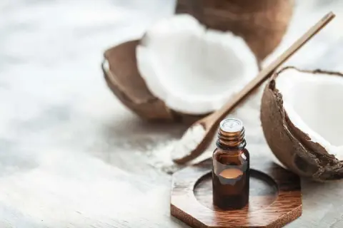 A small bottle of coconut oil sits near a halved coconut and a wooden spoon with coconut flakes. This image prompts the question: is coconut oil safe for cats?