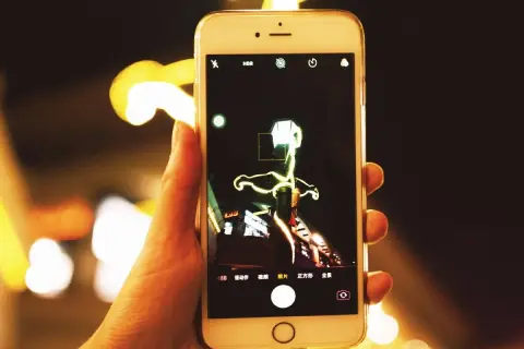 Dłoń trzyma smartfon, na ekranie którego widać interfejs aparatu. Można tu zobaczyć, jak zmienić aparat w telefonie, wybierając różne tryby fotografowania.