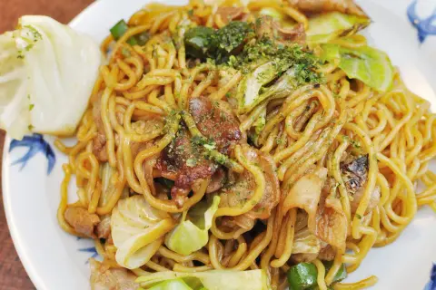 Yaki soba mit Schweinefleisch und Kohl, garniert mit grünen Kräutern. Ein köstliches Gericht, das zum Genießen einlädt.