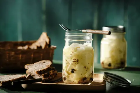 Kohlrabi fermentieren: Gläser mit eingelegtem Kohlrabi, Gewürzen und Brot im Hintergrund.