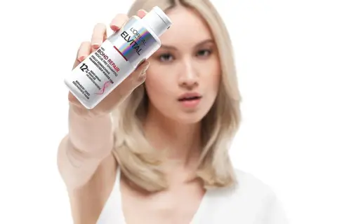 Frau zeigt L'Oréal Elvital Bond Repair Pre-Shampoo gegen extrem trockene Haare. Vorher-Nachher-Effekt für geschädigtes Haar.