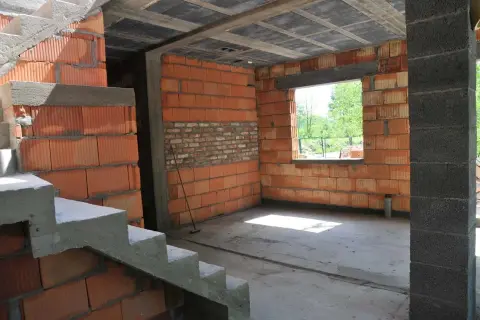 Budowa domu z budynku gospodarczego w toku. Widać schody, ściany z pustaków ceramicznych i betonowe słupy.