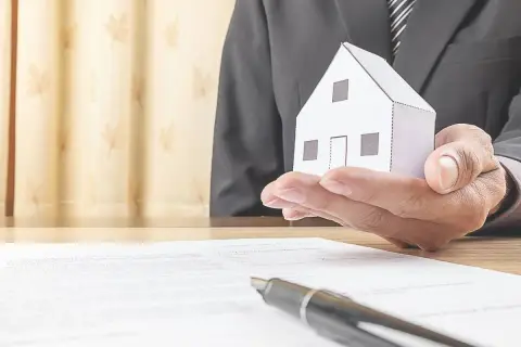 Un uomo in giacca e cravatta tiene una casetta di carta, simbolo di un accordo di leasing immobiliare per privati.