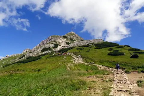 Kamienna ścieżka prowadzi na zielony zbocze, gdzie widać grupę turystów zmierzających na Giewont szczyt.