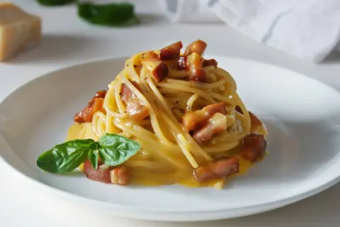 Spaghetti carbonara – przepis oryginalny ze śmietaną. Pyszne danie z makaronem, boczkiem i kremowym sosem jajeczno-serowym, udekorowane bazylią.