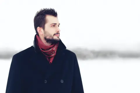Mężczyzna w granatowym płaszczu i czerwonym, wzorzystym szaliku, na tle zimowego krajobrazu. Idealny przykład, jaki szalik do granatowego płaszcza.