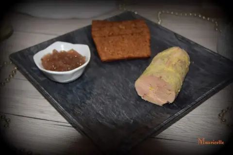 Un morceau de foie gras, une compotée de fruits et une tranche de pain d'épices sur une assiette. La cuisson du foie gras à l'eau bouillante est une méthode délicate.