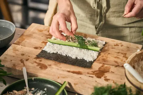 Händer lägger dill på egen sushi med ris, gurka och nori.