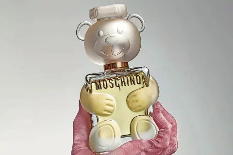 Różowe rękawiczki trzymają uroczy flakon perfum Moschino Toy 2 w kształcie misia.