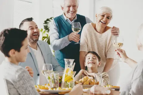 Radosny dzień rodziny przy stole. Dziadkowie, rodzice i dzieci śmieją się, wznosząc kieliszki z winem.