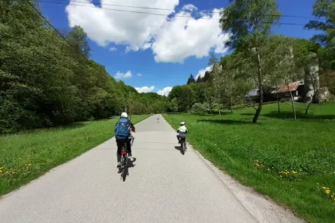 Dwie osoby na rowerach przemierzają malownicze **ojcowskie park narodowy trasy rowerowe**. Słoneczny dzień, zieleń i chmury na niebie.