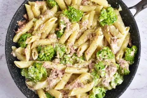 Penne z tuńczykiem i brokułami w kremowym sosie śmietanowo-serowym, przygotowane w czarnej patelni.