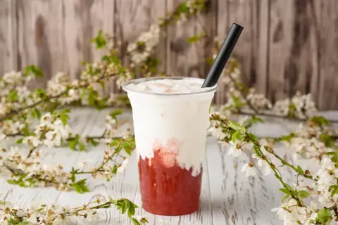 Jak zrobić bubble tea? Pyszny napój z truskawkowym syropem i mleczną pianką, ozdobiony kwitnącymi gałązkami.