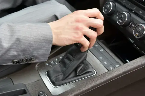 Pierwsza jazda automatem. Dłoń w garniturze zmienia bieg w samochodzie.