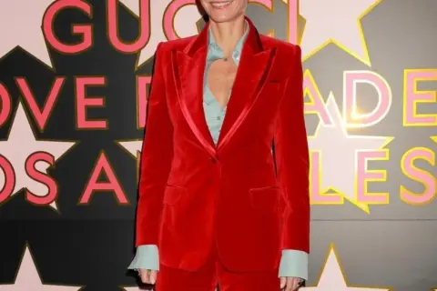 Gwyneth Paltrow in un completo rosso di velluto, sorride davanti a uno sfondo con stelle e lettere rosa e oro.