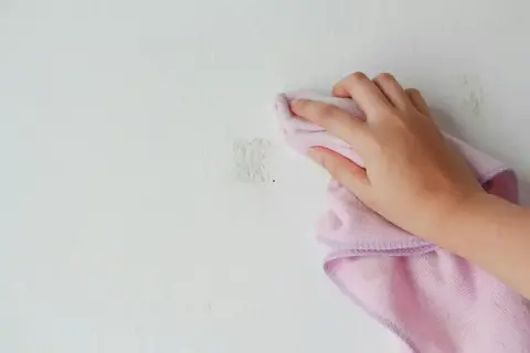 Handen torkar bort klisterrester från en målad vägg med en rosa trasa.