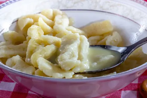 Miska pełna pysznych, domowych klusek kładzionych polanych śmietaną. Łyżeczka nabiera porcję tych delikatnych kluseczek.