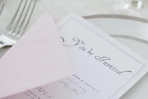 Eleganckie zaproszenie z napisem "You're Invited" i różową kopertą. Wskazówka, jak pisać na zaproszeniu z osobą towarzyszącą.