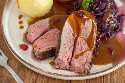 Saftiges Rehschulter Rezept: Rosa gebratenes Fleisch mit Sauce, Rotkohl und Klößen auf einem Teller.