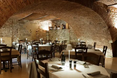 Interno di un ristorante con tavoli apparecchiati, soffitto a volta in mattoni e pareti in pietra. Un'atmosfera accogliente, ideale per scoprire i migliori ristoranti di Verona.
