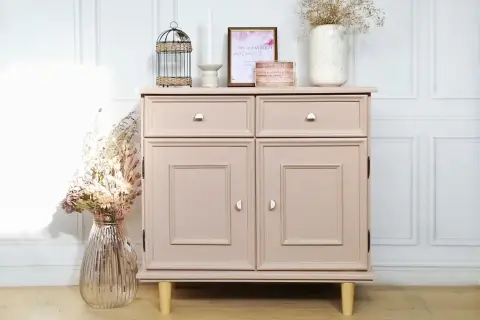 Meuble bas rose poudré, fraîchement repeint, avec deux tiroirs et deux portes. Décoré de fleurs séchées et d'une cage décorative.