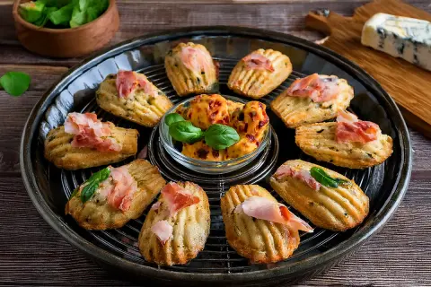 Délicieuses madeleines salées pour apéritif, garnies de jambon cru et de basilic. Parfaites pour une recette facile et gourmande.