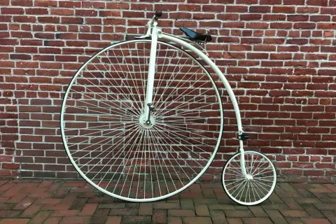 Ein Hochrad, ein Meilenstein in der Entwicklung Fahrrad, steht vor einer roten Ziegelwand.