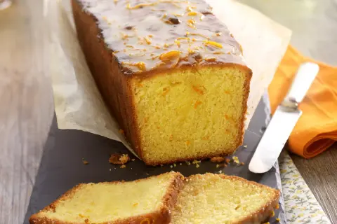Wilgotne ciasto pomarańczowe z błyszczącą glazurą i kandyzowanymi skórkami pomarańczy, pokrojone na kromki.