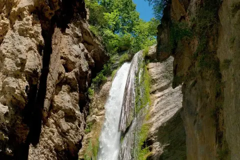 La chute de la druise, une cascade spectaculaire, dévale une falaise rocheuse verdoyante, entourée par la végétation luxuriante et le ciel bleu.