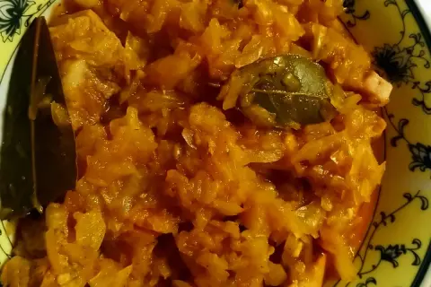 Pyszny bigos ze słodkiej kapusty, z dodatkiem liści laurowych, w żółtej misce z ozdobnym wzorem.