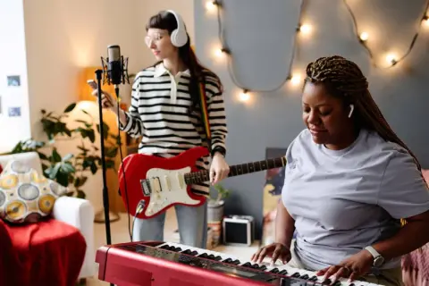 Dwie kobiety tworzą muzykę: jedna gra na keyboardzie, druga na gitarze. Słychać idealną harmonię instrumentów.
