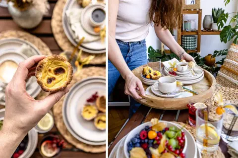 Hand hält ein knuspriges Pastel de Nata. Auf einem Tablett warten weitere Törtchen, Beeren und Kaffee.