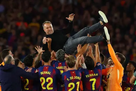 Piłkarze FC Barcelona 22/23 unoszą trenera Xaviego w geście radości po wygranym meczu.