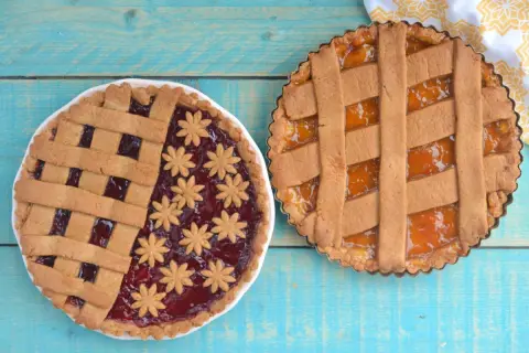 Due crostate senza uova, una con marmellata di frutti rossi e decorazioni a fiore, l'altra con marmellata di albicocche.