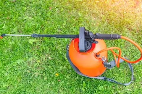 Pomarańczowy opryskiwacz ciśnieniowy na zielonej trawie, gotowy do użycia. Szukasz najlepszego preparatu na chwasty w trawie? Ranking pomoże Ci wybrać!