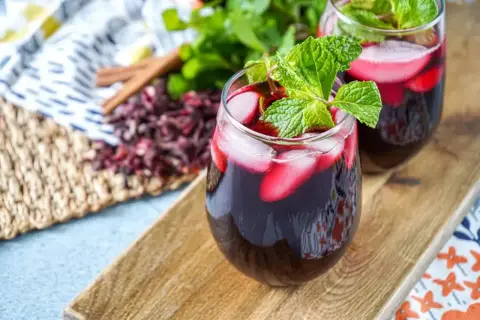 Deux verres de kinkeliba et bissap glacés, garnis de menthe fraîche, sur un plateau en bois.