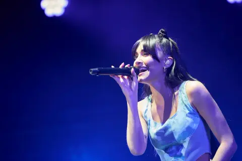 Aitana Zaragoza canta con pasión en un concierto, iluminada por luces azules.