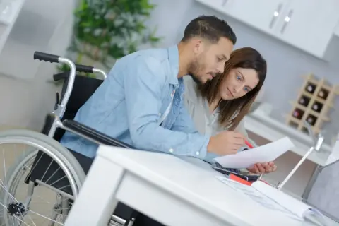Para w wózku inwalidzkim i kobieta analizują dokumenty. Wspólnie wypełniają wniosek o niepełnosprawność druk, szukając wsparcia.