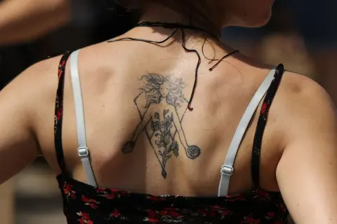 Tatuaz znak zodiaku na plecach kobiety, przedstawiający postać z kwiatami w geometrycznej ramie.