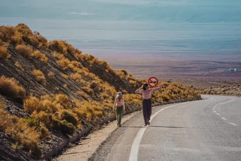 Dwie dziewczynki w kolorowych ubraniach idą pustynią Atacama. Jedna z nich trzyma znak zakazu ruchu.