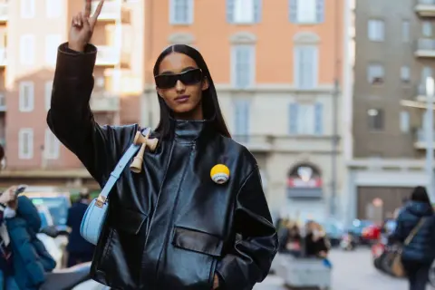 Mona Tougaard, con occhiali da sole e giacca di pelle, fa il segno della pace. Indossa una borsa azzurra e un distintivo giallo.