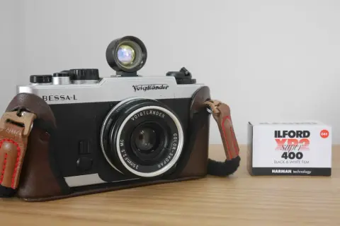 A silver and black Voigtlander Bessa-L camera in a brown leather case sits next to a box of Ilford XP2 Super 400 black and white film.