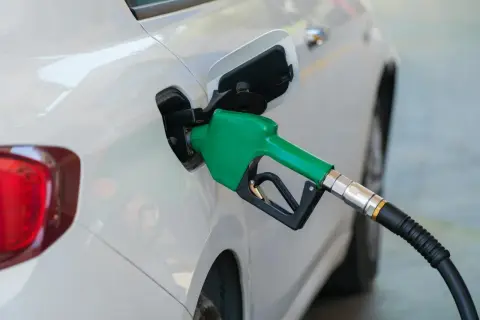Zielona dysza dystrybutora paliwa wlewa płyn do białego samochodu. Dylemat: benzyna czy diesel?